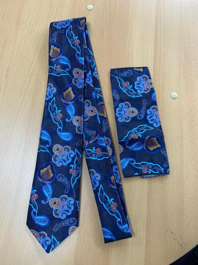 Cravate et pochette bleu motif floral sur table en bois